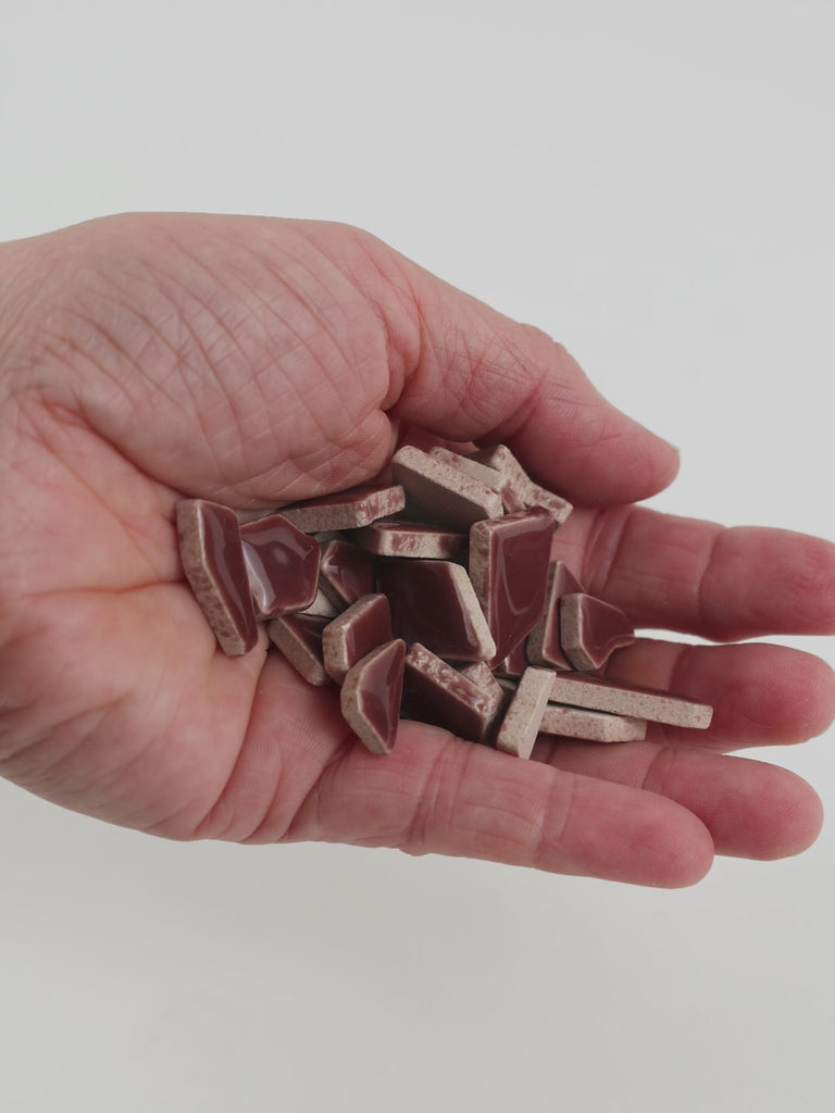 Video of Flip ceramic puzzle pieces in mocha, opaque glazed porcelain, 4–20 mm, held in a hand and poured out to show their shapes and finish