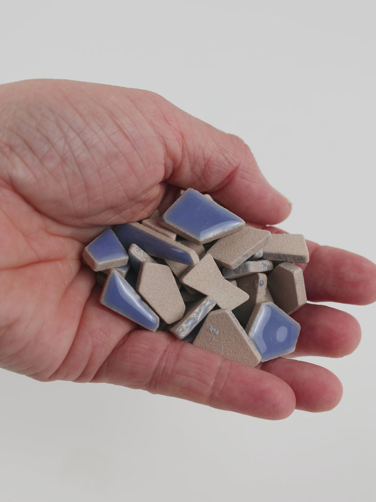 Video of Flip ceramic puzzle pieces in foxglove, opaque glazed porcelain, 4–20 mm, held in a hand and poured out to show their shapes and finish