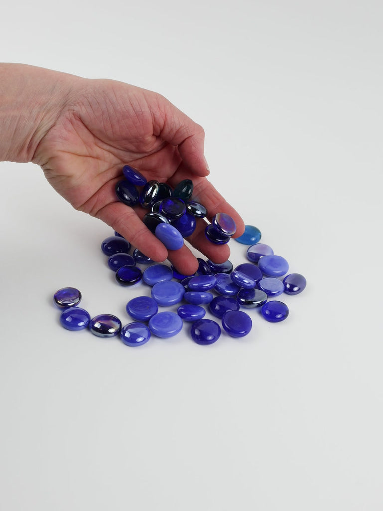 Video of blue mix glass nuggets in cobalt, violet-blue and light blue shades with an iridescent sheen, 16–20 mm, picked up from a pile by hand and dropped back to show their size, round shape and shine