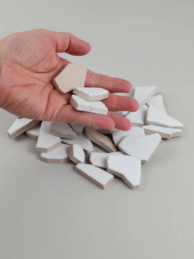Video of Flip XL ceramic puzzle pieces in white, opaque glazed porcelain, 20–60 mm, picked up from a pile by hand and dropped back to show their size, shapes and finish