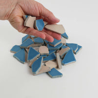 Video of Flip XL ceramic puzzle pieces in Caribbean blue, opaque glazed porcelain, 20–60 mm, picked up from a pile by hand and dropped back to show their size, shapes and finish