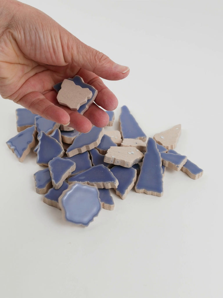 Video of Flip XL ceramic puzzle pieces in foxglove, opaque glazed porcelain, 20–60 mm, picked up from a pile by hand and dropped back to show their size, shapes and finish