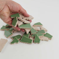 Video of Flip XL ceramic puzzle pieces in reed green, opaque glazed porcelain, 20–60 mm, picked up from a pile by hand and dropped back to show their size, shapes and finish
