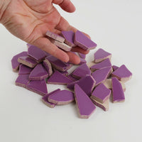 Video of Flip XL ceramic puzzle pieces in purple, opaque glazed porcelain, 20–60 mm, picked up from a pile by hand and dropped back to show their size, shapes and finish