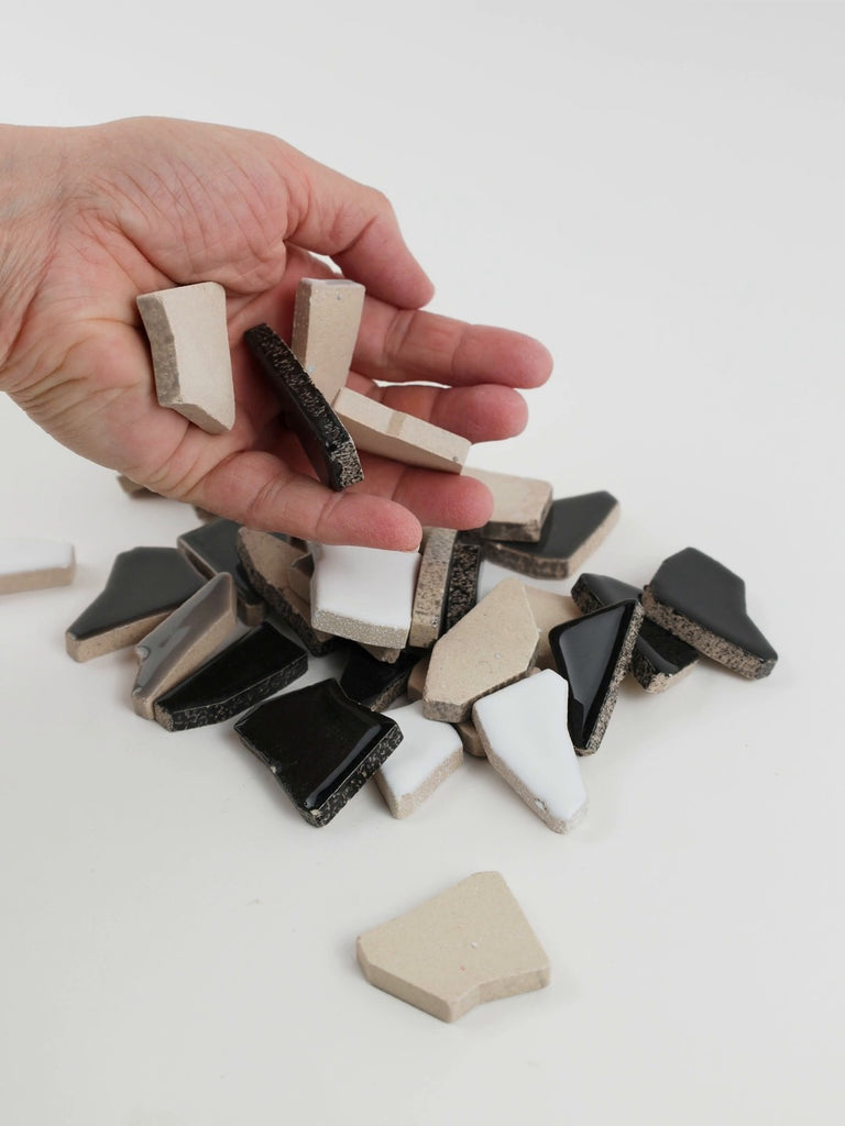 Video of Flip XL ceramic puzzle pieces in grey mix, opaque glazed porcelain, 20–60 mm, picked up from a pile by hand and dropped back to show their size, shapes and finish