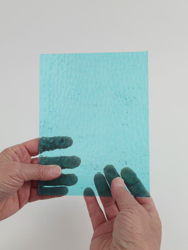 Video of the Water hammered glass plate in hammered transparent blue, 15x19cm, held up and tilted to show its pattern and transparency