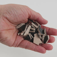 Video of Flip ceramic puzzle pieces in anthracite, opaque glazed porcelain, 4–20 mm, held in a hand and poured out to show their shapes and finish
